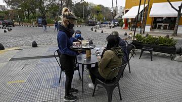 A waitress serves a table placed on a sidewalk in Buenos Aires, Argentina, on August 31, 2020, amid the COVID-19 coronavirus pandemic. - Restaurants and bars reopened on Monday in the city of Buenos Aires after six months of lockdown with tables placed in open-air spaces. (Photo by JUAN MABROMATA / AFP)