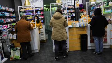 Tres clientes guardan la distancia social en una farmacia de Madrid que cuenta con mamparas protectoras en el mostrador.