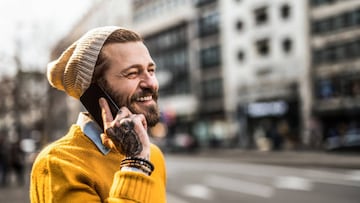 Cheerful tattooed hipster man having a phone conversation in the city.