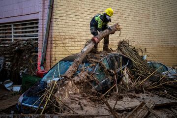 Un bombero retira partes de un árbol que cayó sobre automóviles durante las inundaciones en Masanasa, Valencia.