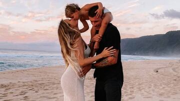 Alana Blanchard, vestida de blanco, da un pico a su hijo Banks mientras abraza a su marido, Jack Freestone (de negro) en una playa de Hawái.