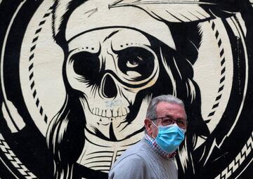 27 April 2020, Spain, Malaga: A man wearing a face mask walks past a graffiti by urban artist D*Face amid the coronavirus crisis.