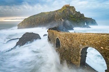 Puente de piedra que conecta tierra firme con la icónica isla-peñón de Gaztelugatxe, situada en la costa de Vizcaya, en el País Vasco. En los últimos años, Gaztelugatxe ha ganado una enorme popularidad mundial por ser uno de los escenarios de la famosa serie de televisión Juego de Tronos, donde fue utilizado como Rocadragón, la fortaleza ancestral de la Casa Targaryen.



