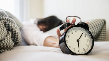 Sleepy woman reaching holding the alarm clock in the morning with late wake up - every day life at home concept