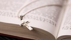 Silver necklace with crucifix cross on christian holy bible book on black wooden table. Asking blessings from God with the power of holiness, which brings luck and shows forgiveness.