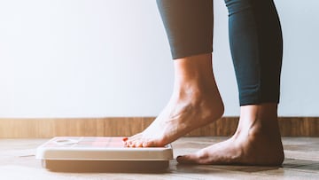 Female checking kilogrammes getting on the scale - self care and body positivity concept - warm flare on left
