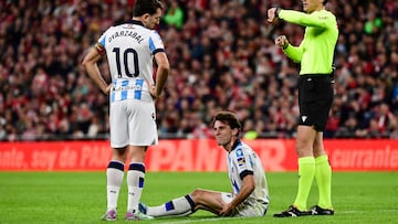 Spanish referee Munuera Montero looks at his watch as Real Sociedad's Spanish defender #02 Alvaro Odriozola sits on the pitch beside Real Sociedad's Spanish midfielder #10 Mikel Oyarzabal during the Spanish league football match between Athletic Club Bilbao and Real Sociedad at the San Mames stadium in Bilbao on January 13, 2024. (Photo by ANDER GILLENEA / AFP)