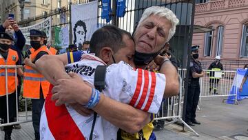 Soccer fans of rival soccer teams Boca Juniors, right, and River Plate, left, embrace as they wait to enter the presidential palace to see Diego Maradona lying in state in Buenos Aires, Argentina, Thursday, Nov. 26, 2020. The Argentine soccer great who led his country to the 1986 World Cup title died Wednesday at the age of 60. (AP Photo/Debora Rey)