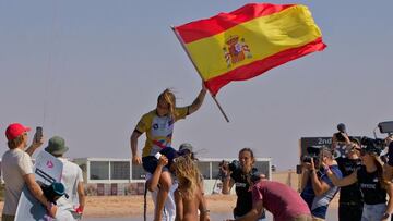 Claudia Le&oacute;n, a hombros de su padre y con la bandera espa&ntilde;ola en la mano, tras ganar la prueba del GKA Kite World Tour 2022 en Arabia Saud&iacute;, el 22 de octubre del 2022. Con fot&oacute;grafos y surfistas documentando la gesta de la kitesurfista espa&ntilde;ola. 