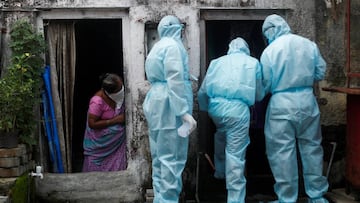 A woman watches as healthcare workers wearing personal protective equipment (PPE) check the temperature of residents of a slum during a check-up camp for the coronavirus disease (COVID-19) in Mumbai, India June 17, 2020. REUTERS/Francis Mascarenhas TP
