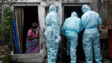 A woman watches as healthcare workers wearing personal protective equipment (PPE) check the temperature of residents of a slum during a check-up camp for the coronavirus disease (COVID-19) in Mumbai, India June 17, 2020. REUTERS/Francis Mascarenhas     TP