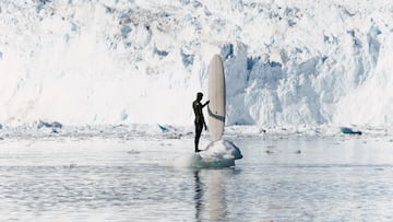 Eurico Romaguera con su tabla de surf frente a un glaciar en Ilulissat, Groenlandia, en verano del 2024.