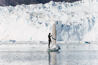 Eurico Romaguera con su tabla de surf frente a un glaciar en Ilulissat, Groenlandia, en verano del 2024.