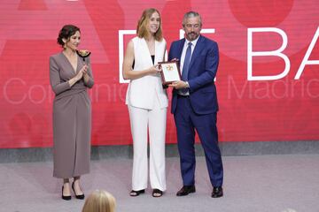 La presidenta de la Comunidad de Madrid, Isabel Díaz Ayuso (i), entrega la Gran Cruz de la Orden del Dos de Mayo al presidente del Club Estudiantes de Baloncesto, Ignacio Triana (d), y a la jugadora Begoña de Santiago (c). 
