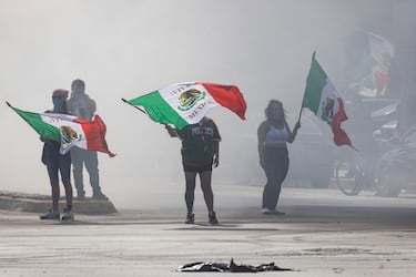 Manifestantes con banderas mexicanas se cubren del humo en Alondra Boulevard durante un enfrentamiento con las fuerzas del orden este domingo en Paramount, California.