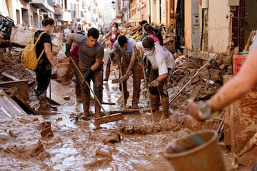 Voluntarios y vecinos ayudan a limpiar el barro de la calle tras las fuertes lluvias en Paiporta, cerca de Valencia.