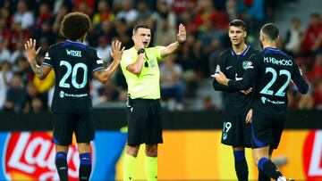 Michael Oliver atiende al árbitro de VAR mientras los futbolistas del Atlético reclaman penalti.