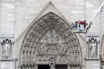 Varios bomberos trabajan en un elevador junto a la fachada de la catedral de Notre Dame