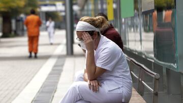Una trabajadora sanitaria con mascarilla se sienta en un banco.