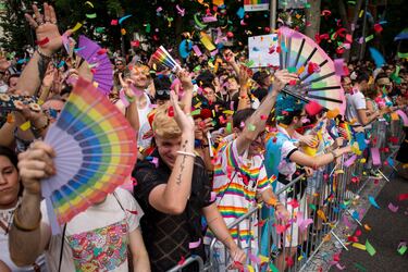 Varios asistentes con abanicos de colores del arcoíris bailan mientras les lanzan papeles durante la gran marcha del Orgullo celebrada en el Paseo del Prado de Madrid. La marcha de este año en Madrid tuvo como lema "20 años promoviendo derechos: Ni un paso atrás".