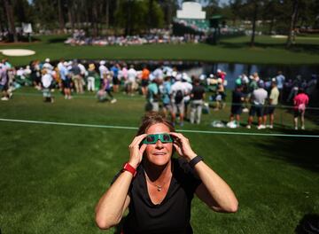 Una aficionada, , con gafas protectoras para ver el eclipse solar, observan el eclipse solar durante el Masters de Augusta.