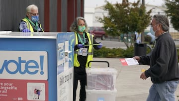 Los trabajadores electorales del condado de King, Jules James, a la izquierda, y Diana Antrim, a la derecha, observan c&oacute;mo un votante deja una boleta en un buz&oacute;n, el martes 27 de octubre de 2020.