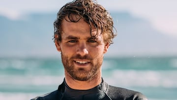 Graham Howes con el pelo mojado y traje de neopreno mirando a cámara en una foto tipo retrato, con el mar de fondo.