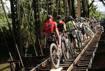 Los ciclistas cargan con la bicicleta mientras atraviesan un puente ferroviario en la localidad de Limón. 