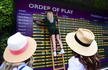 Una azafata completa los cuadrantes del orden de juego del campeonato de Wimbledon, mientras los asistentes a la gran cita del tenis sobre hierba contemplan su proceder. Esperemos que la chica sepa mantener el equilibrio sobre la escalera de mano mientras realiza su tarea.