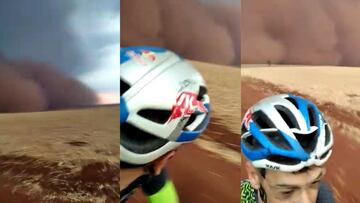 Un ciclista con casco Red Bull y bici MTB se gira para mirar la tormenta de arena gigante que le persigue. 