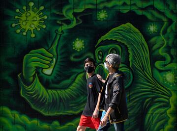 A man and a boy wearing face masks walk past a COVID-19 graffiti in Barcelona on April 26, 2020 amid a national lockdown to prevent the spread of the coronavirus.