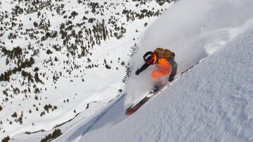 Abel Moga, freerider de la Val d'Aran, levantando nieve polvo con sus esquís y una chaqueta naranja, casco y mochila anti avalanchas en la montaña.