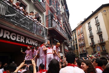 Una persona vierte agua desde un balcón a los asistentes durante la inauguración del festival de San Fermín.