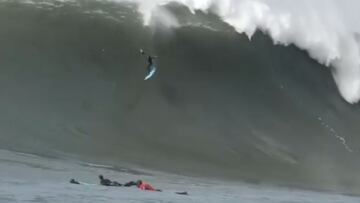 Grant 'Twiggy' Baker literalmente volando con su tabla de surf azul en una ola gigante en Mavericks mientras otros surfistas se lo miran remando por el lado de esta ola de California, en enero del 2021.