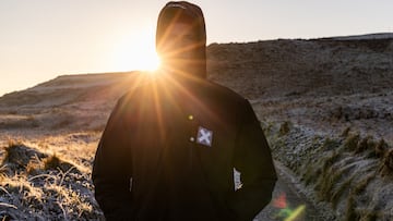 El surfista Tim Elter, con chaqueta Blue Banana, en un camino de Fuerteventura con el sol poniéndose al fondo por detrás de una montaña.