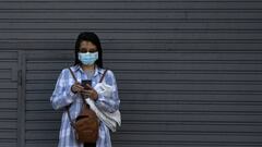 A woman wearing a face mask uses her mobile phone in front of a closed store during the lockdown imposed due to the pandemic of the new coronavirus COVID-19, in Buenos Aires, on April 15, 2020. - Staring from today, it is mandatory in Argentina to use face masks in supermarkets, pharmacies and in the public transport. (Photo by Juan MABROMATA / AFP)