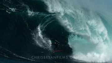 El surfista local Kip Caddy surfeando una ola gigante en Shipstern Bluff, considerada la ola más peligrosa del mundo. En la foto, justo sobre el Devil's Drop con una tabla de surf roja y neopreno, con la ola formando tubo y espuma.