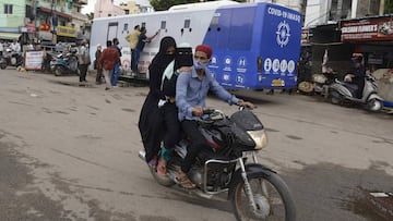 People ride on a motorbike past residents waiting to get their names registered at a free Covid-19 coronavirus testing van in the old city of Hyderabad on August 27, 2020. (Photo by NOAH SEELAM / AFP)