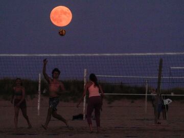 La luna se eleva sobre la playa mientras la gente juega voleibol en la orilla del lago Michigan en Chicago.