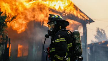 Un bombero se encuentra frente a un edificio en llamas mientras el fuego y el humo se elevan de un incendio forestal en la región del Biobío, donde, según medios locales, múltiples incendios forestales provocaron evacuaciones de emergencia, en Concepción, Chile.
