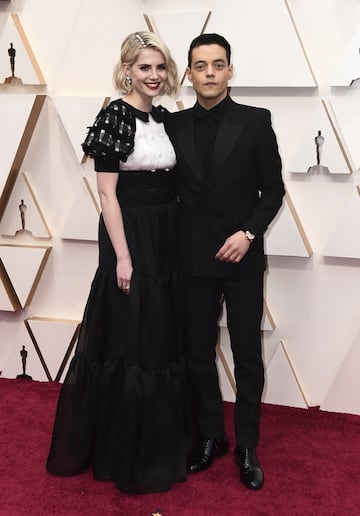 La actriz Lucy Boynton, con un vestido blanco y negro de Chanel, posa junto a su pareja el actor Rami Malek. 