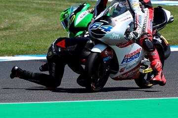 El piloto italiano Mattia Casadei (de negro) se cae durante la primera práctica de la categoría de Moto2 del GP de Australia justo delante del neerlandés Bo Bendsneyder (64). A pesar de la espectacularidad de la acción, ninguno de los dos corredores sufrió daños y pudieron completar las sesiones de entrenamientos.