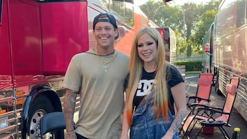 El skater Ryan Sheckler y la cantante Avril Lavigne sonriendo frente a unos autocares y unas sillas.