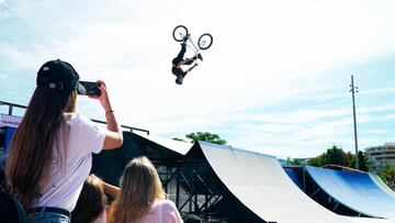 Un rider de BMX tirando un backflip en las rampas del Central Park del Madrid Urban Sports 2021, con dos chicas mirando y haciendo un v&iacute;deo con el tel&eacute;fono m&oacute;vil. 