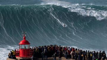 Un surfista surfea una ola gigante frente al Fuerte de San Miguel Arc&aacute;ngel, en Nazar&eacute; (Portugal) mientras decenas de personas se lo mirandesde el faro, durante el mundial de surf tow-in. 