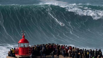 Un surfista surfea una ola gigante frente al Fuerte de San Miguel Arcángel, en Nazaré (Portugal) mientras decenas de personas se lo mirandesde el faro, durante el mundial de surf tow-in.