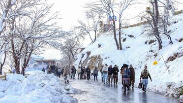 Local tourists walk along a road after a heavy snowfall in Murree, around 70 kilometres (45 miles) northeast of the capital, Islamabad on January 8, 2022 after an incident earlier where at least 21 people died in an enormous traffic jam caused by tens of thousands of visitors thronging to a Pakistani hill town to see unusually heavy snowfall. (Photo by AFP)