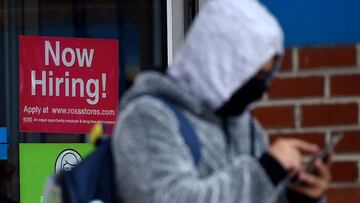 A man wearing a face mask stands next to a &quot;Now Hiring &quot; sign in front of a store on December 18, 2020, in Arlington, Virginia . - US lawmakers were hammering out final details on a major coronavirus relief package and an attached federal fundin
