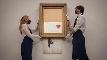 (FILES) In this file photo taken on September 3, 2021 assistants pose alongside an artwork titled x91Love is the Binx92 by British street artist Banksy during a photocall at Sothebyx92s auction house in central London. - A partially shredded canvas of one of British artist Banksy's most celebrated works is expected to sell for millions when it goes under the hammer on October 14. (Photo by Tolga Akmen / AFP) / RESTRICTED TO EDITORIAL USE - MANDATORY MENTION OF THE ARTIST UPON PUBLICATION - TO ILLUSTRATE THE EVENT AS SPECIFIED IN THE CAPTION