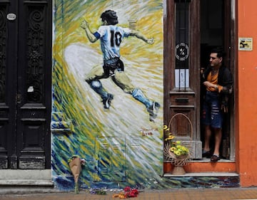 A man looks at flowers left next to a mural depicting Argentine football star Diego Maradona, in San Telmo neighborhood, Buenos Aires